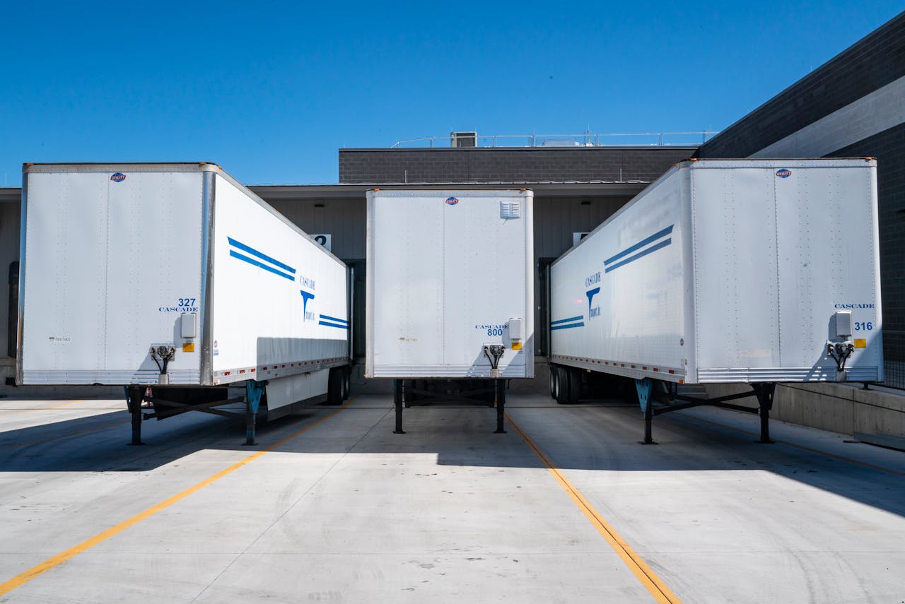 our-story Three white cargo trailers parked at an industrial shipping dock under clear blue skies.